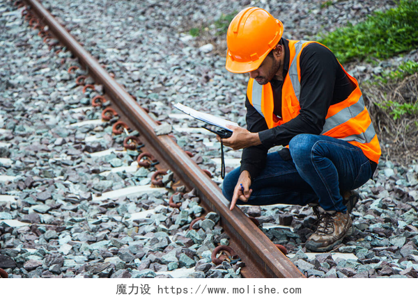 一个在铁路上检查的工人督察工程戴着钢盔和背心,检查铁路轨道上的铁路建设工作.亚洲工人和同事站在旧火车车厢旁边.
